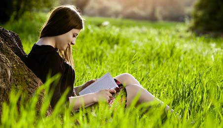 A girl reading a book under a tree in the morning